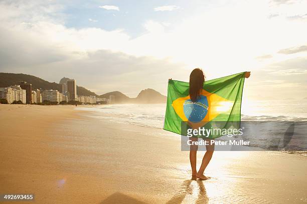 woman holding brazilian flag on copacabana beach, rio, brazil - copacabana imagens e fotografias de stock