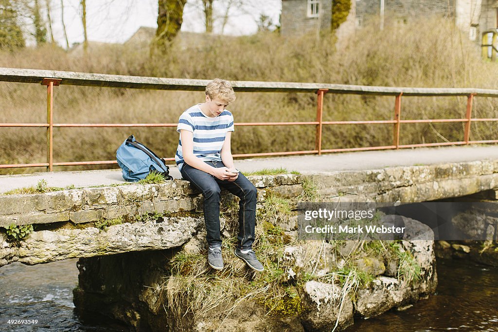 Unhappy teenage boy looking down from rural bridge