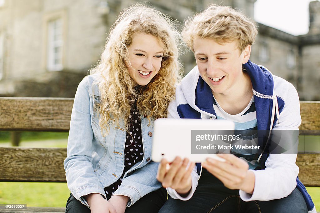 Teenage brother and sister looking at digital tablet on bench