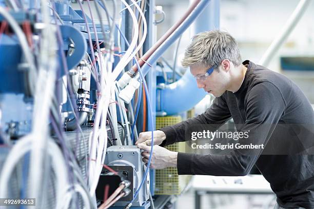 mid adult male technician maintaining cables in engineering plant - kabel stock-fotos und bilder