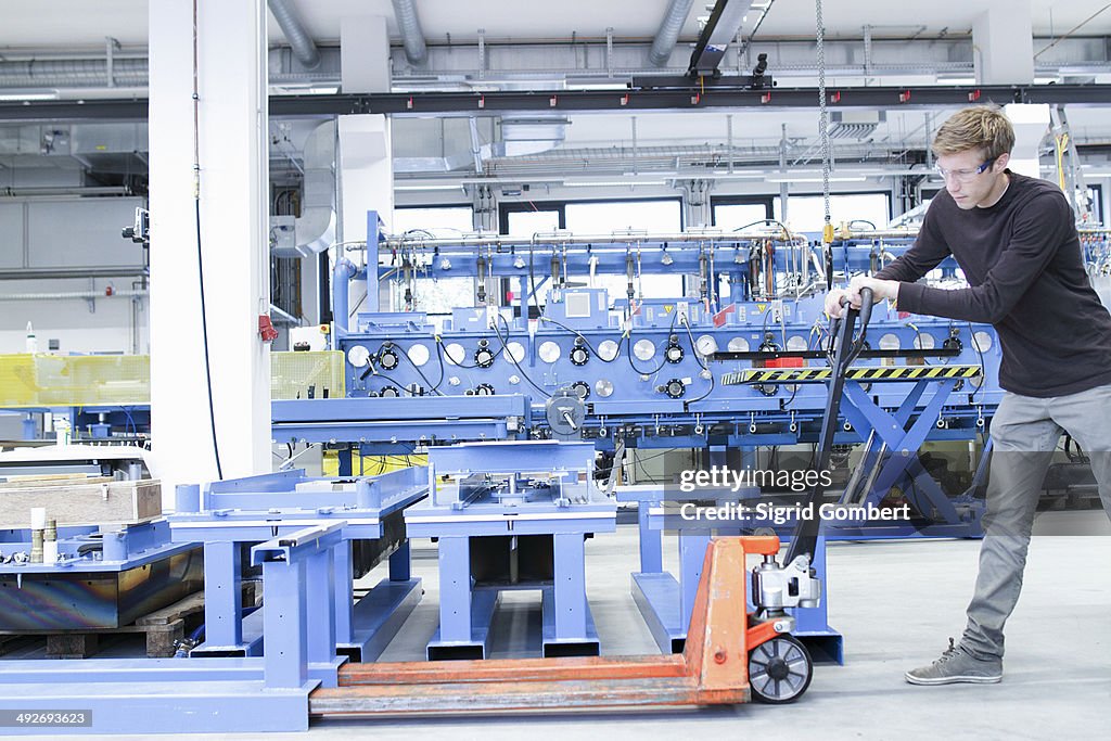 Mid adult male moving products on pallet jack in engineering plant
