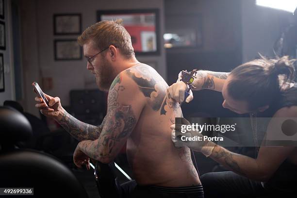 artist tattooing man's back in studio - tatoeage stockfoto's en -beelden
