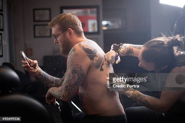 artist tattooing man's back in studio - tattooing stock pictures, royalty-free photos & images