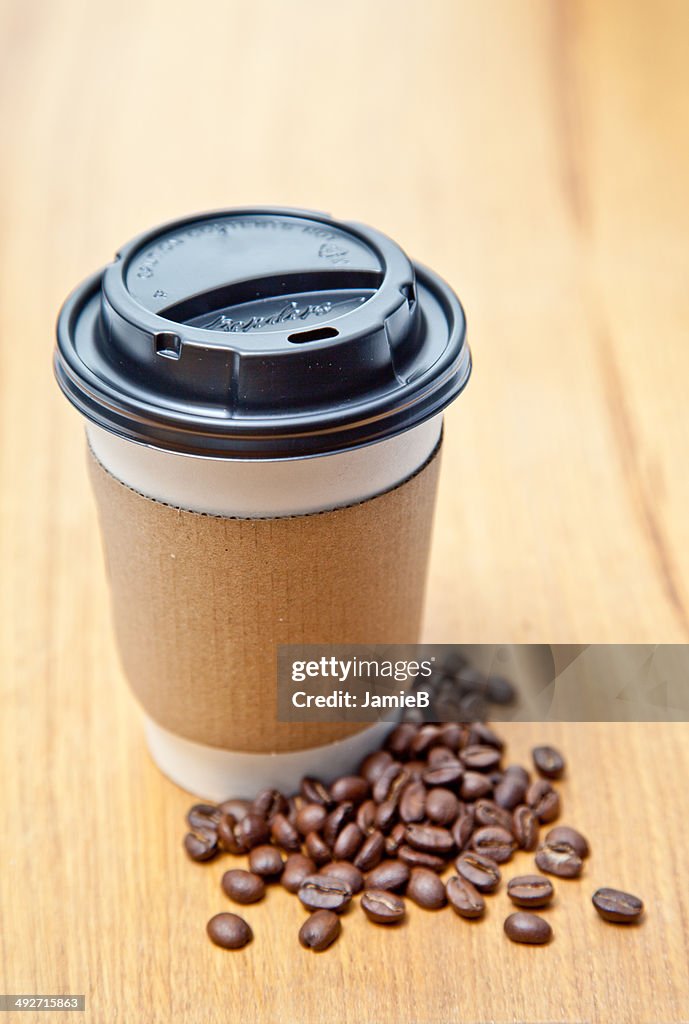 Disposable coffee cup and coffee beans on table