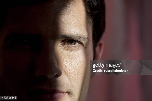 close-up portrait of a man with half face hidden in darkness - hidden identity stock pictures, royalty-free photos & images