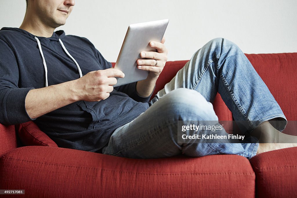 Mid adult man relaxing on sofa looking at digital tablet
