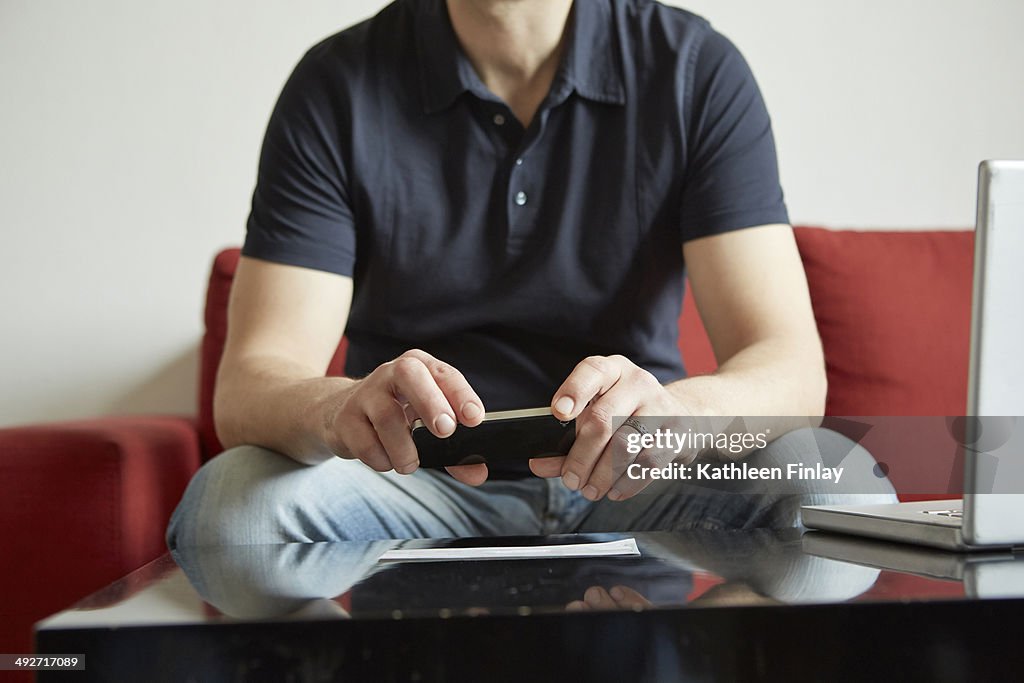 Mid adult man holding smartphone with digital tablet and laptop on table