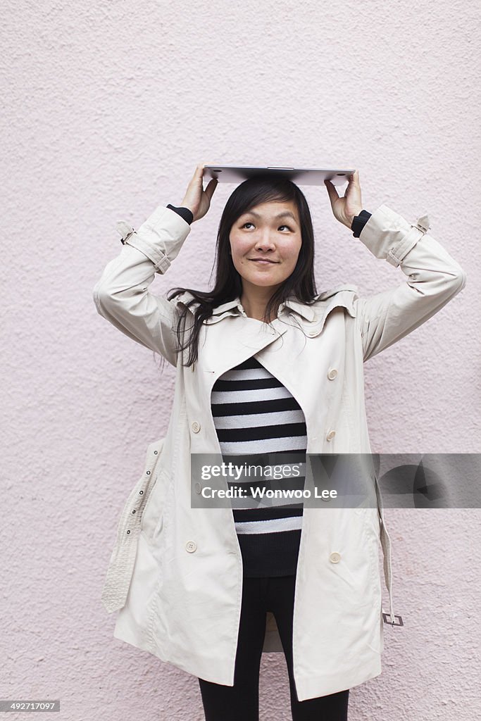 Mid adult woman holding up digital tablet on her head