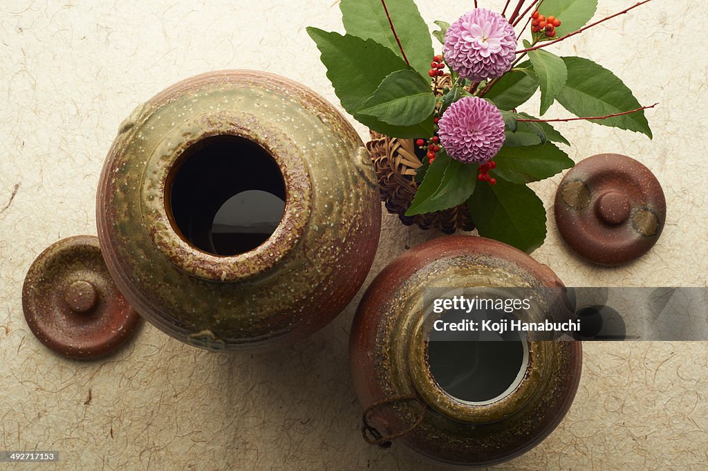 Still life of ceramic jars and lids with vase of flowers and berries