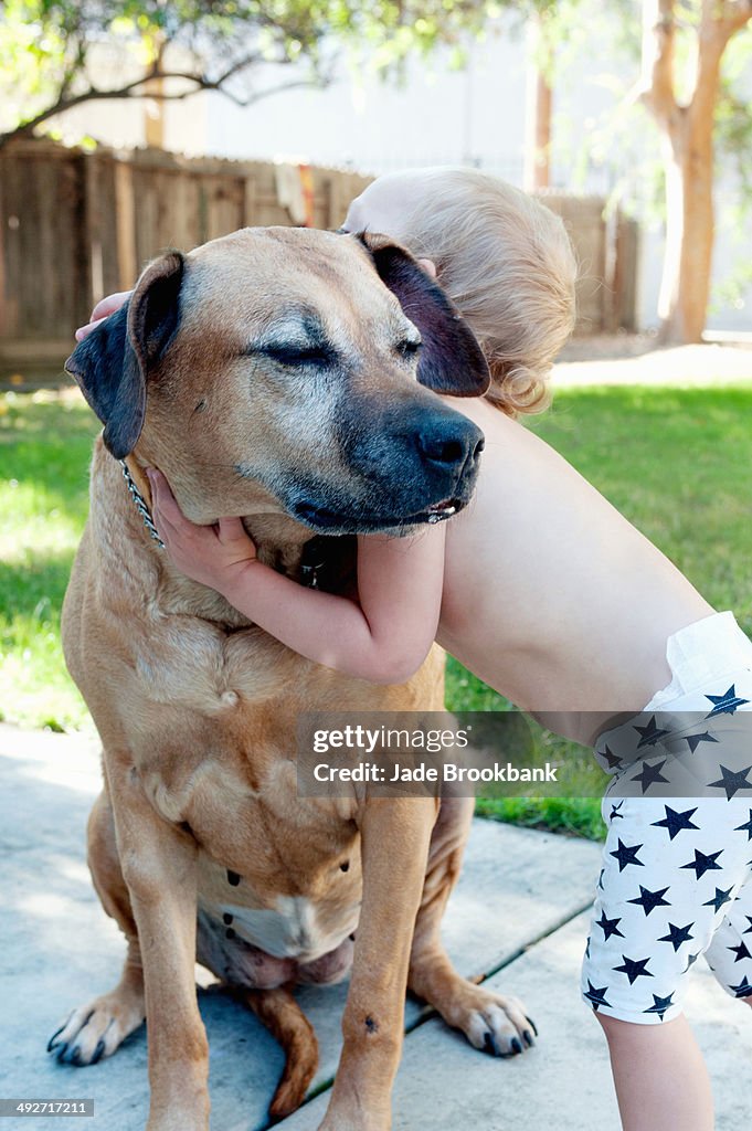 Female toddler hugging old dog