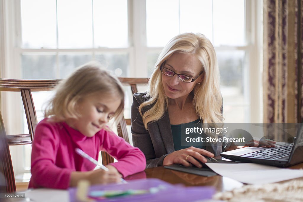 Mother and young daughter doing work and homework in dining room