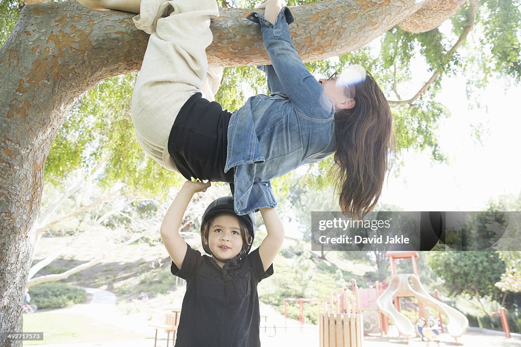 Upside down mother wrapped around tree branch with son helping