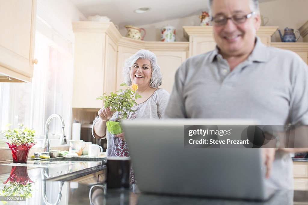 Mature couple in kitchen using laptop