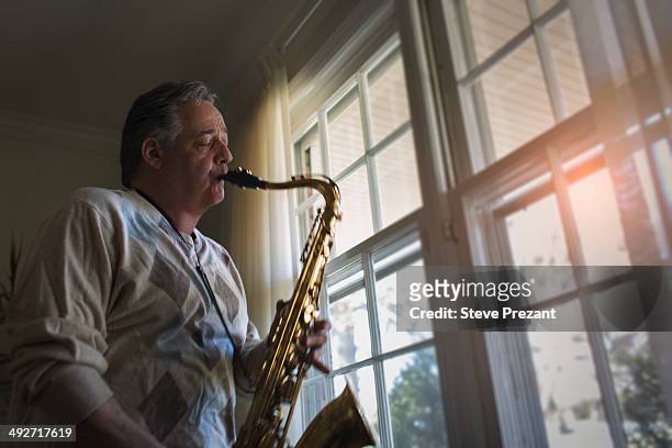 mature man at home playing saxophone - saxophone stock-fotos und bilder