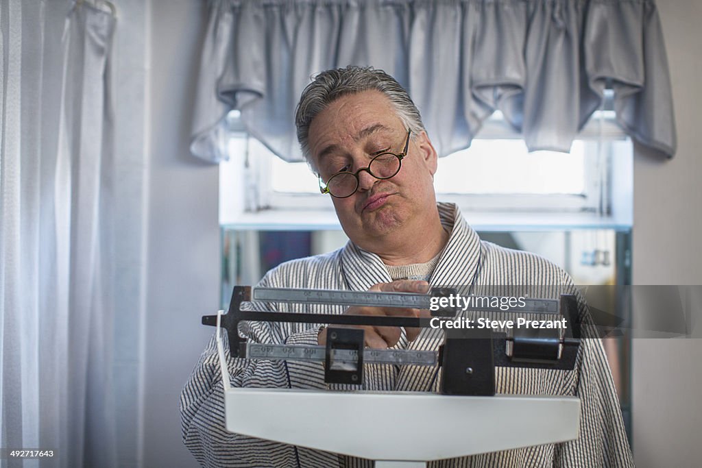 Unhappy mature man on bathroom weighing scales