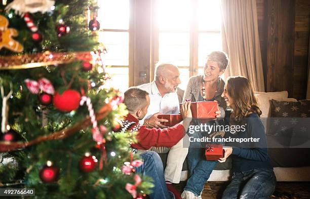 family on the living room exchancing christmas presents - cadeau noel stockfoto's en -beelden