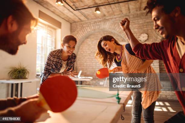 happy businesswomen playing table tennis against businessmen at casual office. - table tennis stock pictures, royalty-free photos & images