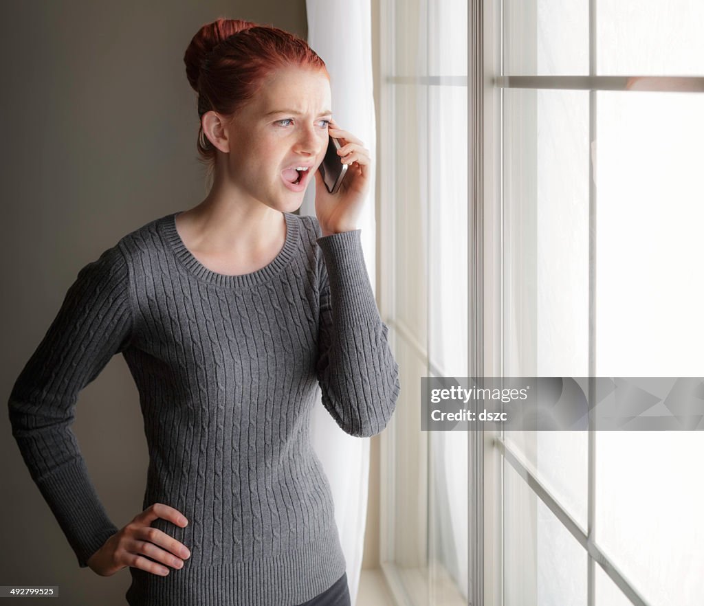 Arrabbiato, contrariato giovane donna gridando su telefono cellulare dalla finestra