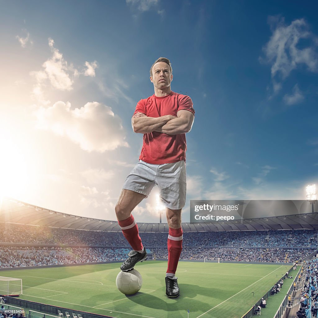 Giant Footballer Standing in Floodlit Soccer Stadium At Sunset