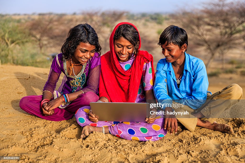 Happy Indian hijos usando computadora portátil, desert village, India