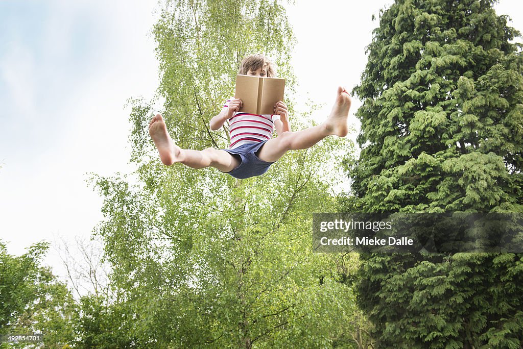 Child reading a book while jumping in the air