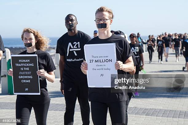 People with black tape on their mouth walk along the Sea Point coast as they attend a protest against human trafficking in Cape Town, South Africa on...