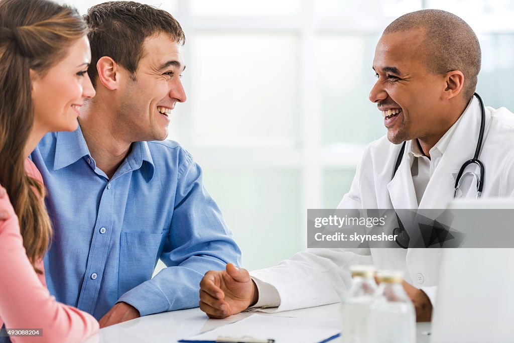 Glückliches Paar sprechen mit afrikanischen amerikanischen Arzt.