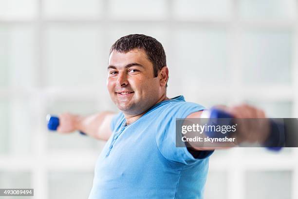 fat man ejercicio con mancuernas y mirando a la cámara. - hombre gordo fotografías e imágenes de stock