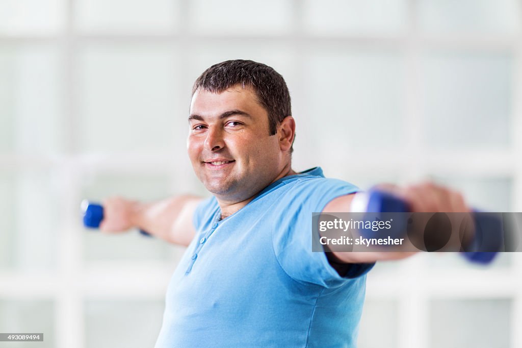Fat man exercising with dumbbells and looking at camera.