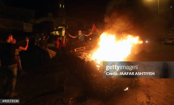 Palestinian youth stand next to a burning car belonging to an Israeli settler, that was set on fire by Palestinians as it entered the northern...
