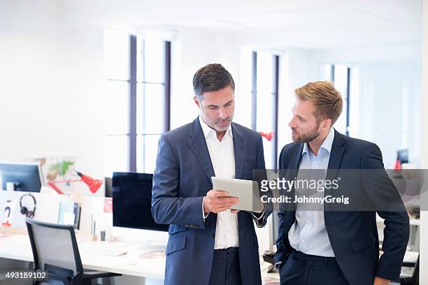 business colleagues in impromptu discussion using digital tablet - meeting candid office suit stockfoto's en -beelden