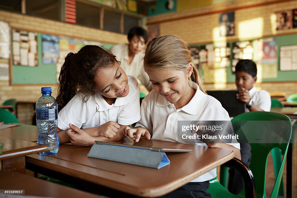 Schoolgirls looking at tablet togther and smiling