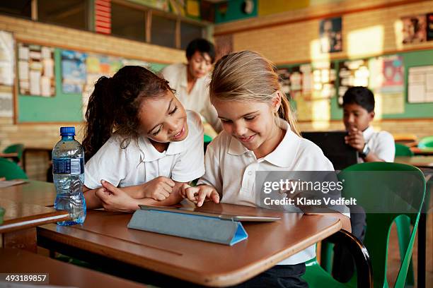 schoolgirls looking at tablet togther and smiling - primary school children in uniform stock pictures, royalty-free photos & images