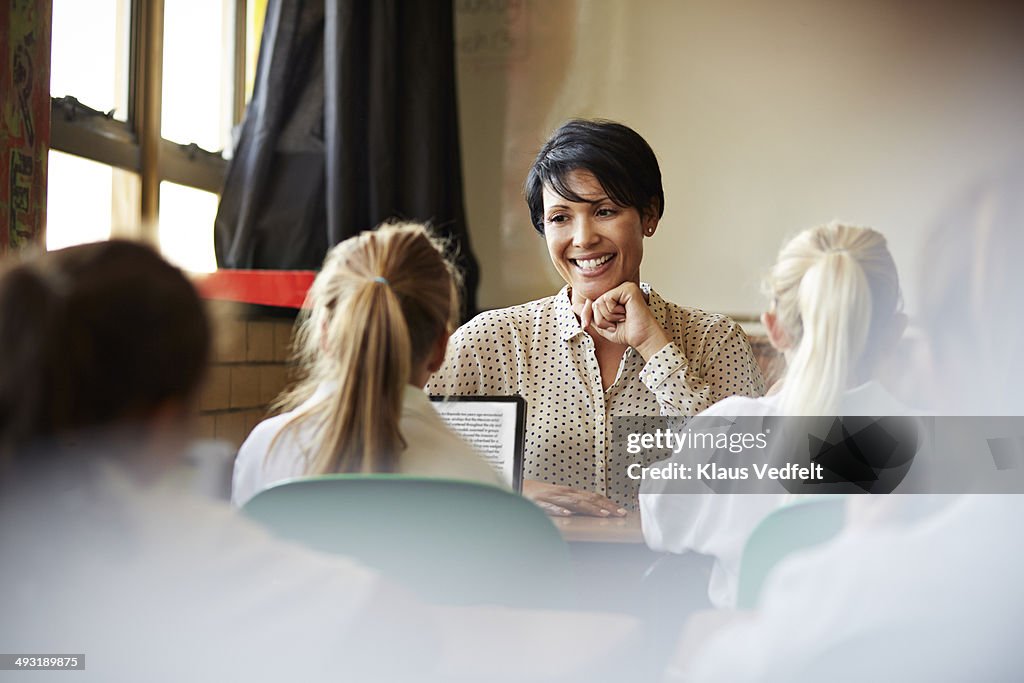 Schoolgirl reading on tablet for teacher in class