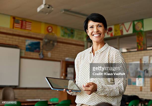teacher in classroom holding tablet - teacher stock-fotos und bilder
