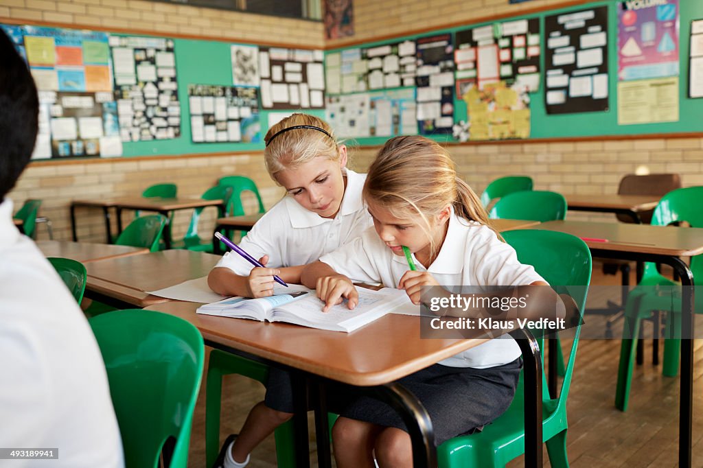 Schoolgirls looking together in book in class