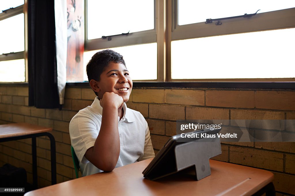 Schoolboy in class laughing with tablet in front