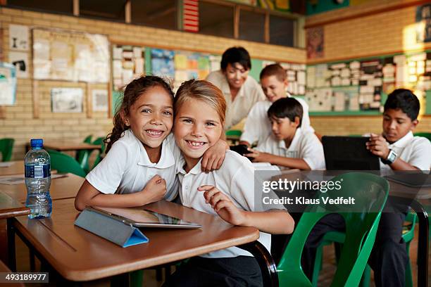 schoolgirls hugging in classroom - boy school uniform stock-fotos und bilder