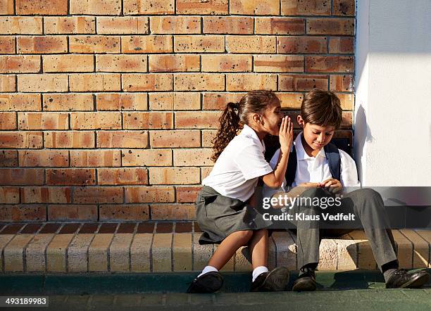 schoolgirl whispering in classmates ear, outside - child whispering stockfoto's en -beelden