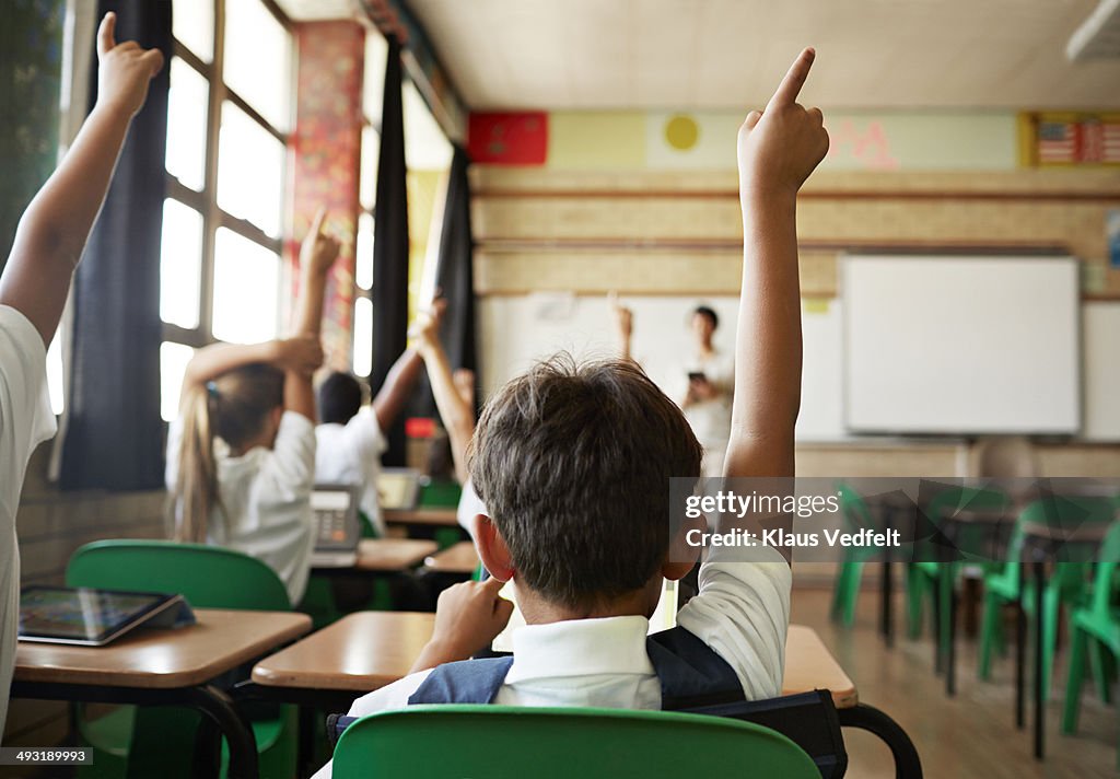 Rear view of boy with raised hand in class