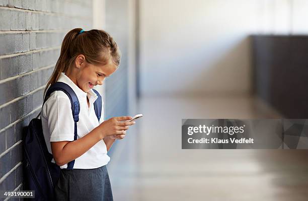 schoolgirl looking at phone and smiling - schüler smartphone stock-fotos und bilder