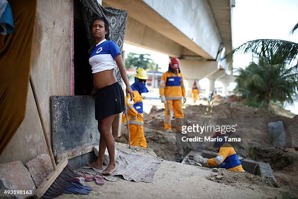 Viviane Sabino de Souza pauses outside her makeshift dwelling next to construction workers on a stretch of the Transcarioca BRT highway being...