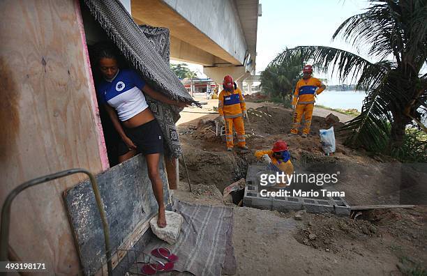 Viviane Sabino de Souza steps out of her makeshift dwelling next to construction workers on a stretch of the Transcarioca BRT highway being...