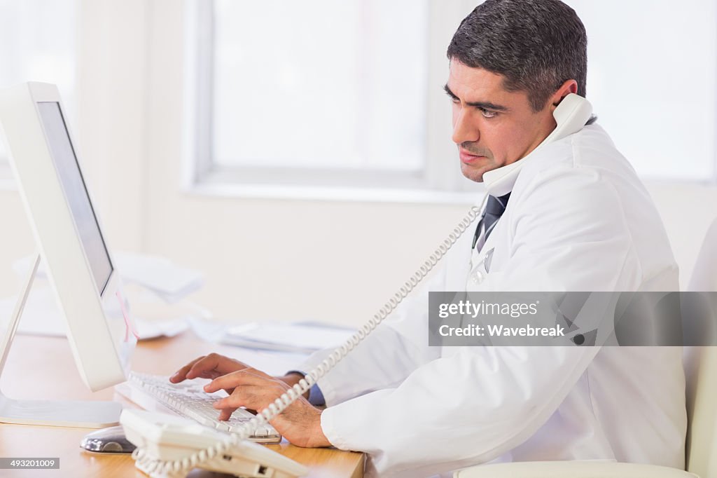 Concentrato maschio medico utilizzando computer e telefono