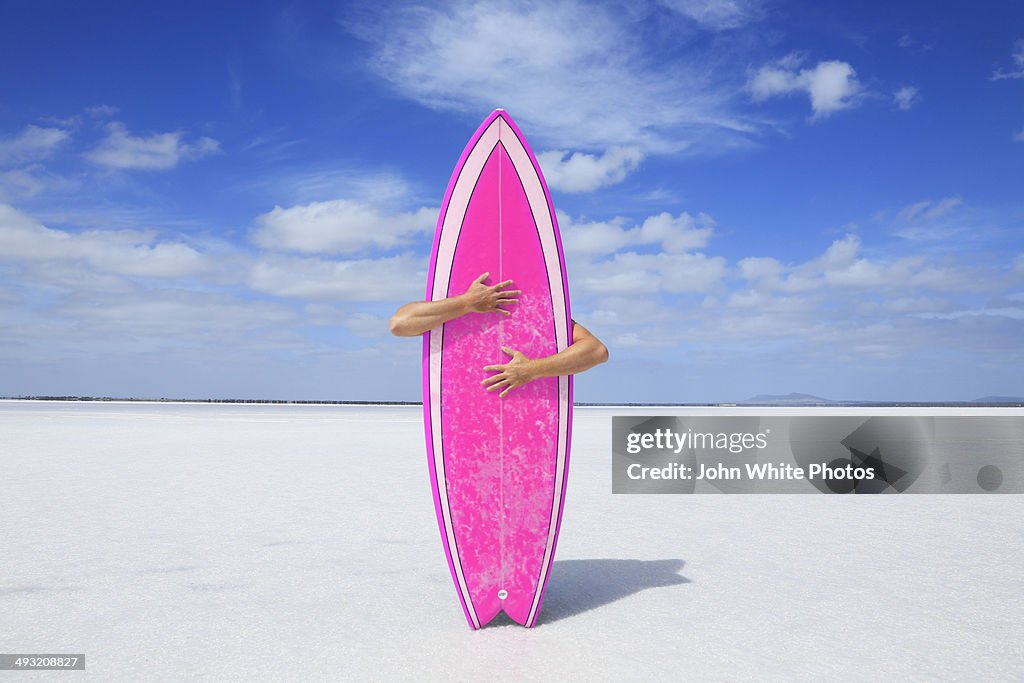 Arms hugging a pink surfboard. Australia.