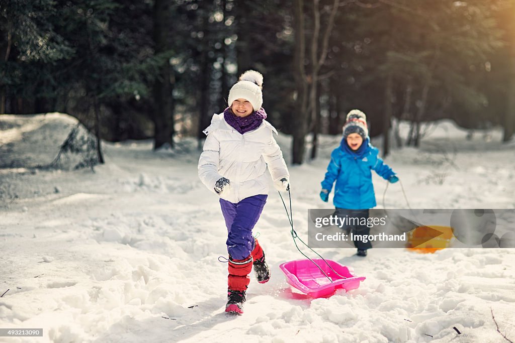 Kids having fun in winter - running with sleds