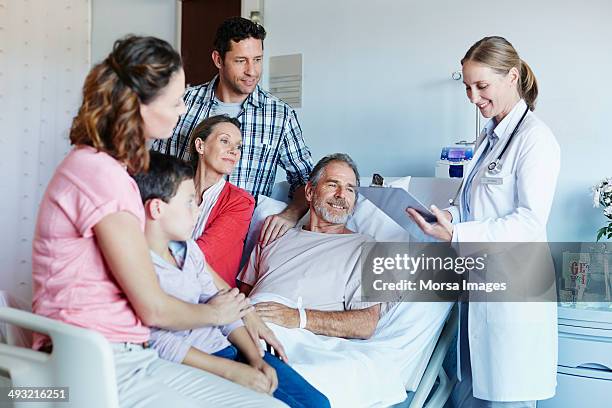 doctor attending ill man with family in ward - child hospital bed stockfoto's en -beelden