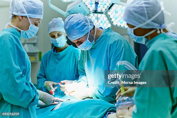 surgeons performing surgery in operating room - cirugía fotografías e imágenes de stock