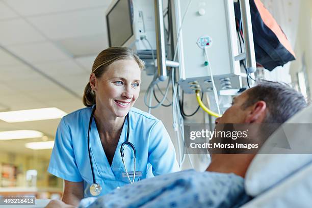 smiling doctor looking at patient in hospital ward - patient foto e immagini stock