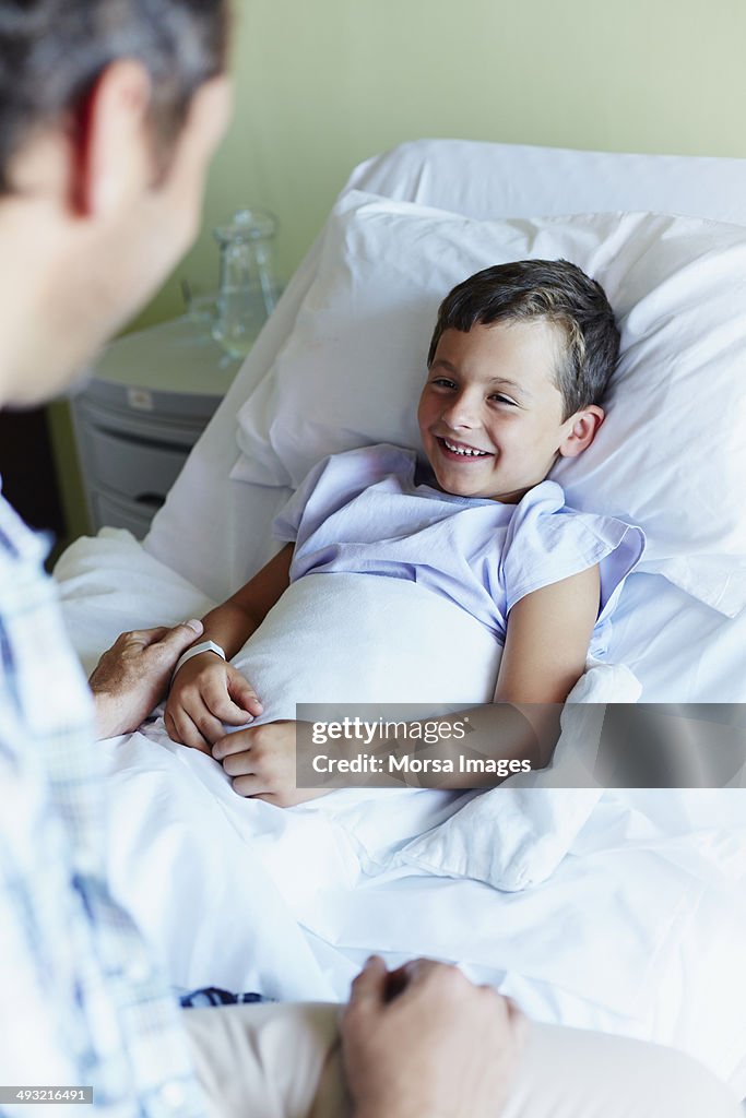 Father with happy son lying in hospital bed